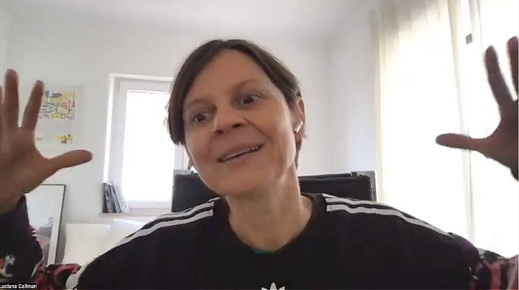 Mulher branca aparece na tela com braços abertos e mãos espalmadas voltadas para a câmera, parece explicar algo